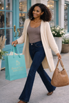 woman wearing an oversized cream knit cardigan with dark bootcut jeans carrying a turquoise shopping bag and brown purse walking outside a boutique with turquoise doors, cozy fall cardigan outfit for women, casual chic boutique style, comfortable layering piece