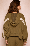 back view of woman wearing an olive boho jacket with crochet detail and relaxed fit on a neutral beige background, lightweight boutique jacket styled for casual everyday outfits