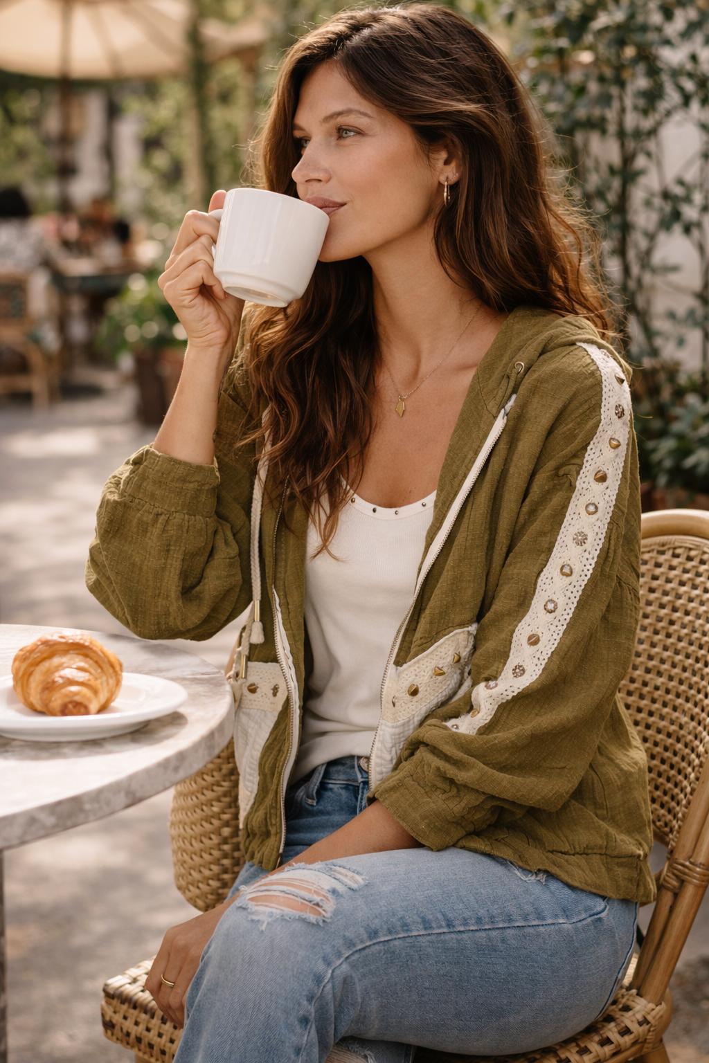 woman sitting at an outdoor café wearing an olive boho jacket with crochet detail styled with jeans and a tank, lightweight boutique jacket for casual everyday outfits and effortless layering