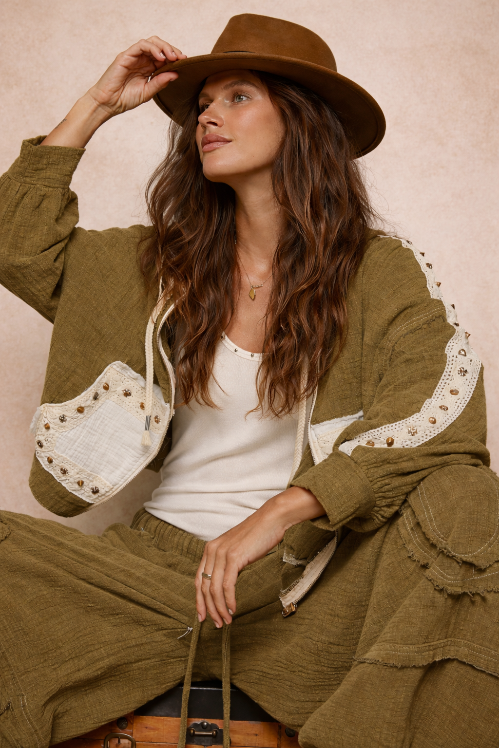 woman wearing an olive boho jacket with crochet detail and relaxed fit styled with a casual outfit on a neutral beige background, lightweight boutique jacket for everyday wear and layering