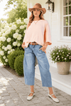 A model wearing a straw hat, light wash denim, and the Peach Oversized Dolman Sleeve Top and flats