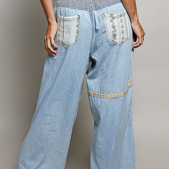 Back view of woman wearing Pol clothing wide leg patchwork jeans with a grey background.
