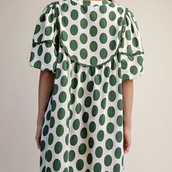 Back view of a woman wearing polka dot linen mini dress with a cream background.