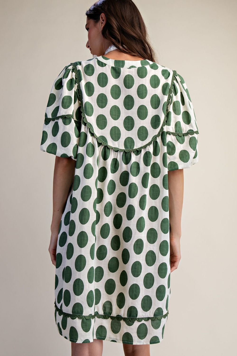Back view of a woman wearing polka dot linen mini dress with a cream background.