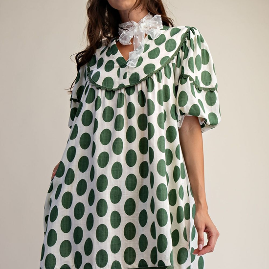 Woman wearing Polka dot linen mini dress that is green and white with a cream background.