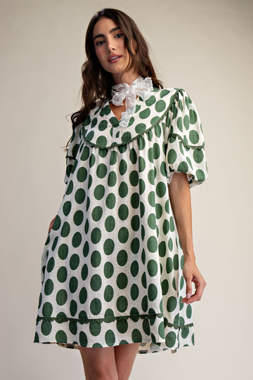 Woman wearing Polka dot linen mini dress that is green and white with a cream background.