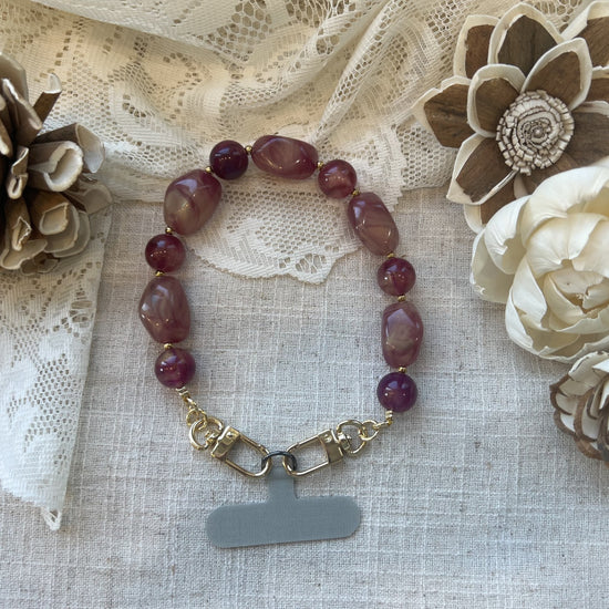 Shimmery berry orchid phone wristlet on a textured neutral background