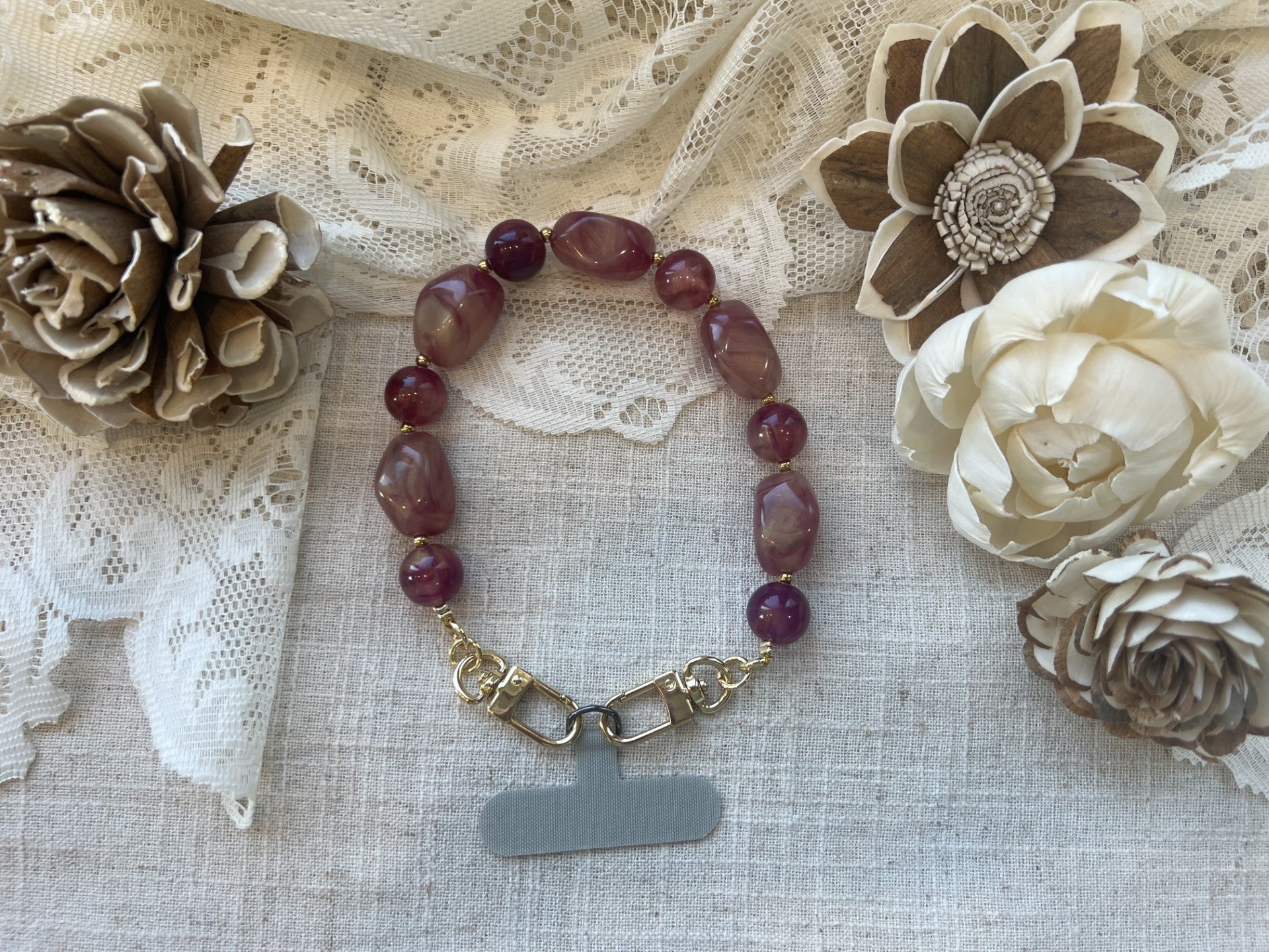 Shimmery berry orchid phone wristlet on a textured neutral background