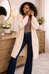 woman wearing a long-oversized cream cardigan with dark bootcut jeans in a cozy getting ready setting, soft knit cardigan for women, casual fall outfit layering piece, boutique boho style cardigan
