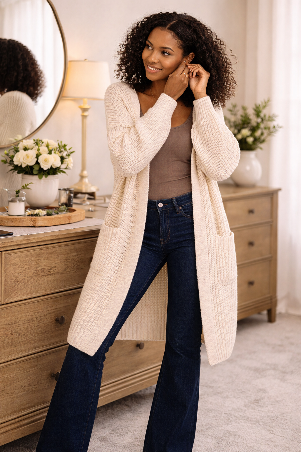 woman wearing a long-oversized cream cardigan with dark bootcut jeans in a cozy getting ready setting, soft knit cardigan for women, casual fall outfit layering piece, boutique boho style cardigan