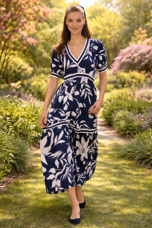 Woman walking through a blooming spring garden wearing a navy and white floral maxi dress with a flowing silhouette in soft natural sunlight