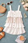 flat lay of white tiered mini dress with floral detail and button front on muted teal background with boutique accessories, lightweight boho summer dress styled for warm weather outfits and everyday wear