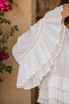 Close-up detail of the Aria Crinkled Ruffle Top featuring dramatic layered bell sleeves, delicate lace trim accents, and lightweight crinkled white fabric in a rustic boho-inspired outdoor setting.