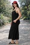 Side view of women's black wide-leg cropped jumpsuit with spaghetti straps styled with flat sandals outdoors