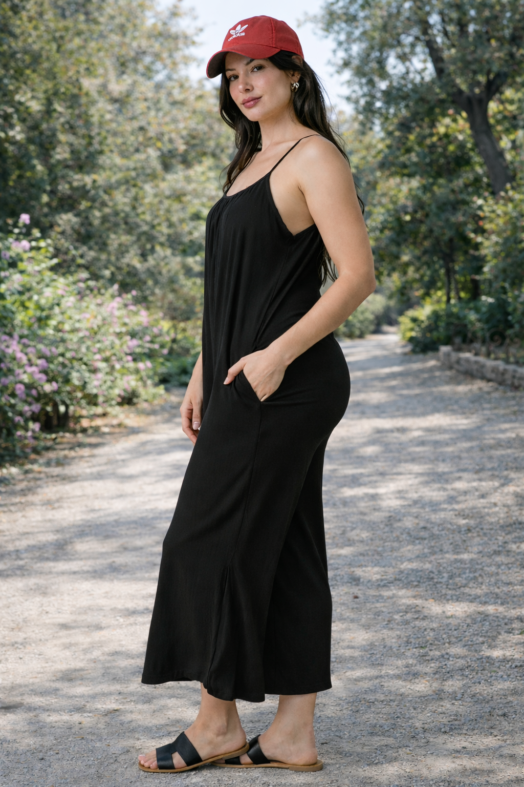 Side view of women's black wide-leg cropped jumpsuit with spaghetti straps styled with flat sandals outdoors