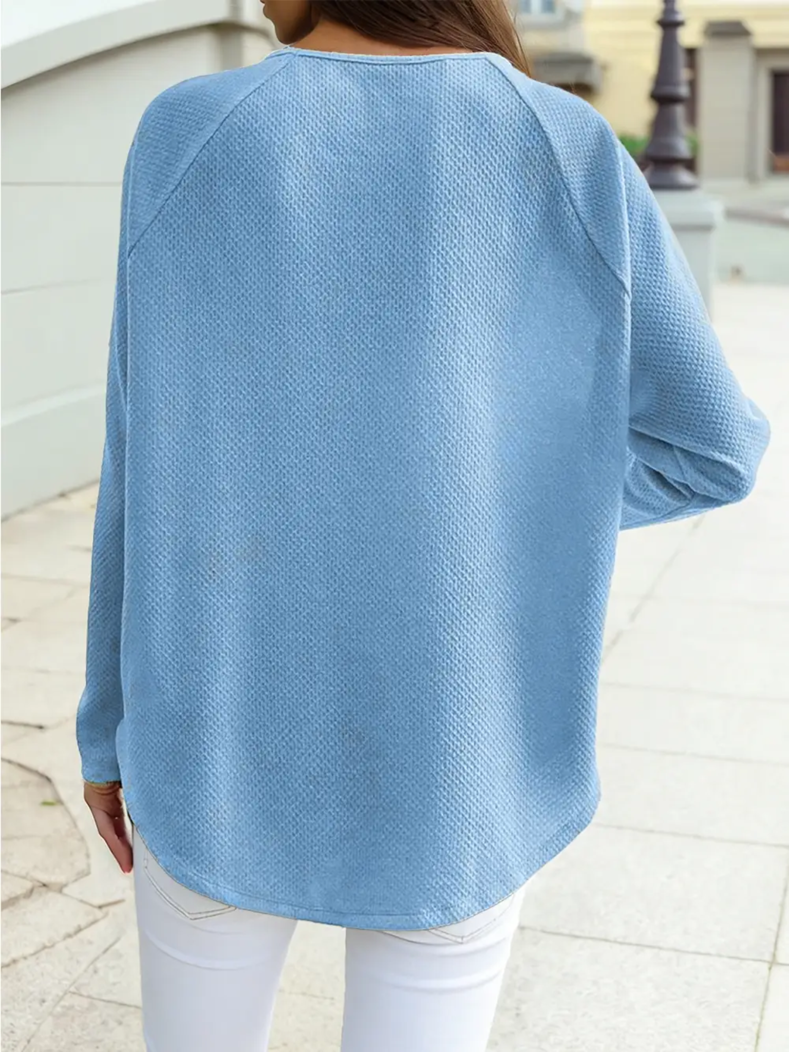 Back view of a soft blue textured jacquard shift top with relaxed fit and long sleeves styled with white jeans for an everyday casual look