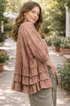 woman wearing a dusty rose BlueVelvet boho embroidered ruffle kimono with eyelet details, styled with sage green pants in a soft outdoor garden setting