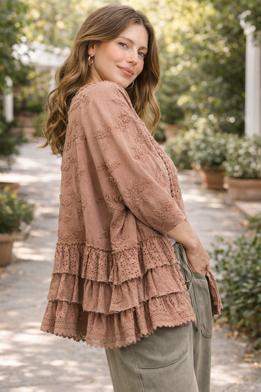 woman wearing a dusty rose BlueVelvet boho embroidered ruffle kimono with eyelet details, styled with sage green pants in a soft outdoor garden setting