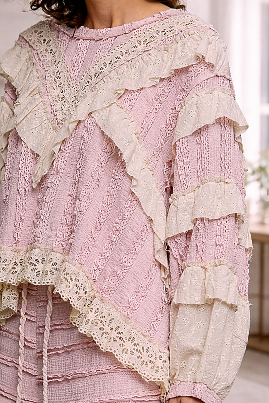 Close-up of blush pink boho lace ruffle top with cream eyelet detailing and layered textures, styled in a soft neutral interior setting