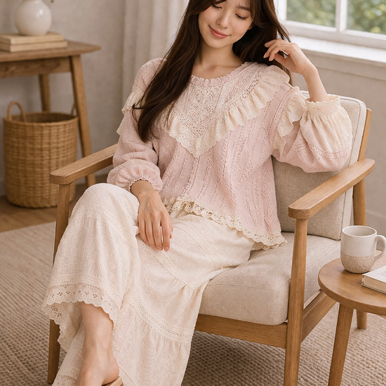 Woman seated in woven chair wearing blush pink boho lace ruffle top and cream wide leg pants, holding a mug in a soft neutral cozy interior