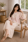 Woman seated in woven chair wearing blush pink boho lace ruffle top and cream wide leg pants, holding a mug in a soft neutral cozy interior