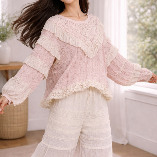 Woman twirling in blush pink boho lace ruffle top and cream wide leg pants in a soft neutral indoor setting, showcasing flowy movement and texture