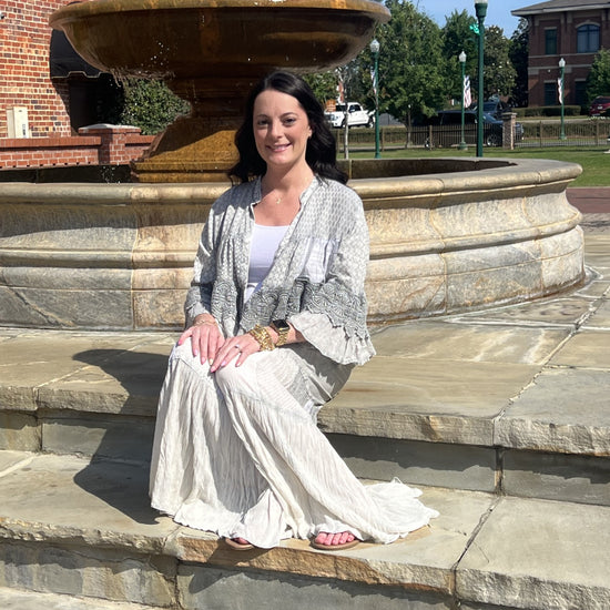 Woman sitting on stone steps wearing the Boho patchwork lace ruffle shrug and Grey boho tiered patchwork pants.