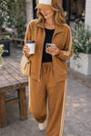 Woman wearing caramel stripe athleisure jacket and wide leg lounge pants set checking phone with coffee in relaxed coffee shop lifestyle outfit