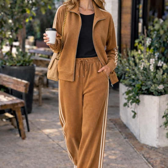 Woman walking with coffee wearing caramel wide leg track pants and stripe athleisure jacket set styled with sneakers and trucker hat in casual coffee run outfit