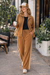 Woman walking with coffee wearing caramel wide leg track pants and stripe athleisure jacket set styled with sneakers and trucker hat in casual coffee run outfit