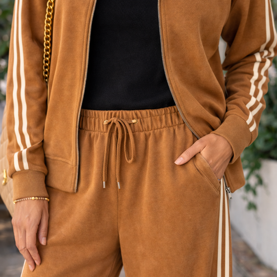 Detail view of caramel wide leg lounge pants featuring drawstring waistband and cream stripe track detail styled with matching athleisure jacket