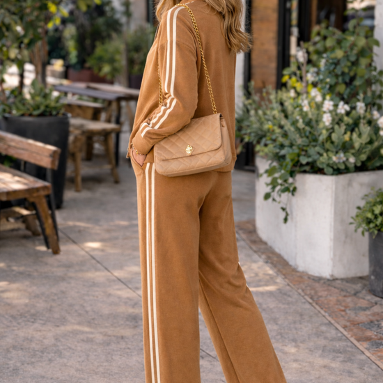 Side view of caramel wide leg stripe track pants women athleisure lounge set outfit styled with sneakers and trucker hat in casual street style setting