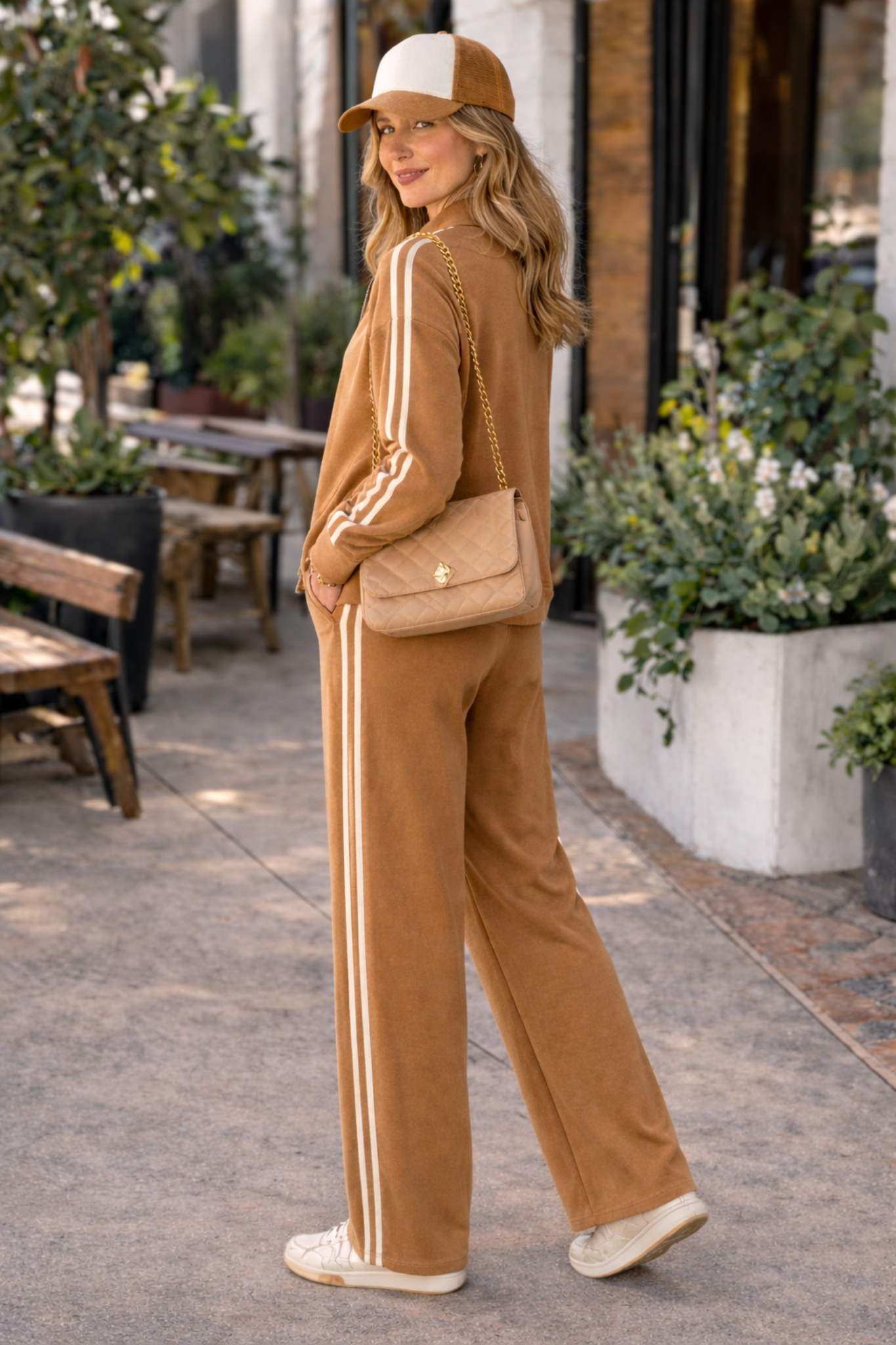 Side view of caramel wide leg stripe track pants women athleisure lounge set outfit styled with sneakers and trucker hat in casual street style setting