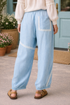 Back view of chambray patchwork joggers with lace trim pocket and elastic waistband, styled with cream boho blouse outside boutique with turquoise doors