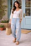 Woman wearing chambray patchwork joggers with white lace tank and beige cardigan, styled with woven sandals and tote outside boutique with turquoise doors