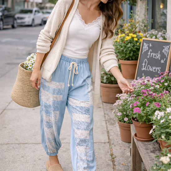 Woman wearing chambray patchwork joggers with lace trim tank and cardigan, walking and picking flowers at outdoor market in relaxed boho style