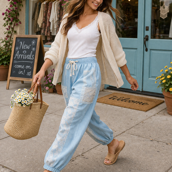 Woman walking in chambray patchwork joggers with white tank and beige cardigan, carrying straw tote outside boutique in relaxed boho style