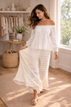 woman twirling in cream boho lace wide leg pants with off shoulder blouse in a soft sunlit boutique setting