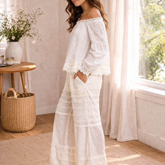 side view of woman wearing cream boho lace wide leg pants with off shoulder blouse in a soft sunlit boutique setting