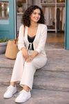 Woman sitting outside a boutique wearing a cream knit cardigan and wide leg pants set styled with a black camisole, white sneakers, and gold jewelry