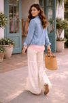 woman walking away wearing cream lace wide leg pants with blush boho blouse and denim jacket outside boutique with teal doors