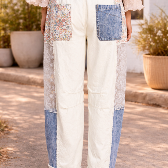 Back view of cream patchwork pants with floral, lace, and denim panels styled with a soft boho blouse and tan leather sandals in a sunlit boutique courtyard