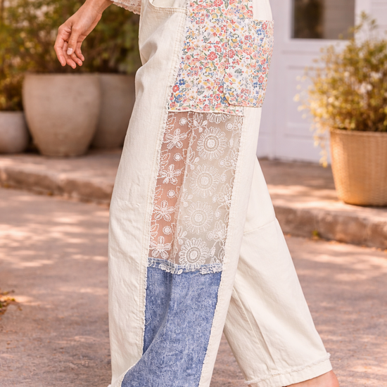 Side view of cream patchwork pants with floral and lace panels styled with a flowy boho blouse and tan leather sandals in a sunlit boutique setting