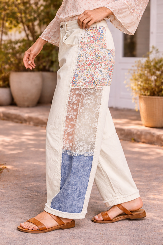 Side view of cream patchwork pants with floral and lace panels styled with a flowy boho blouse and tan leather sandals in a sunlit boutique setting