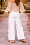 back view of woman wearing distressed white wide leg jeans with flowy off the shoulder boho blouse and flat sandals outdoors