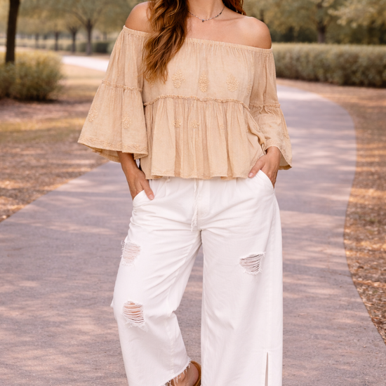 woman wearing distressed white wide leg jeans with off the shoulder boho blouse and sandals walking outdoors on a sunny path