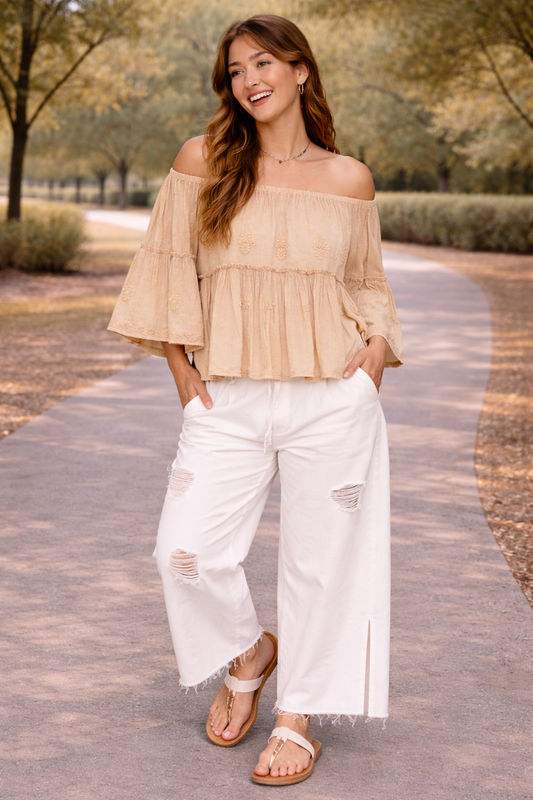 woman wearing distressed white wide leg jeans with off the shoulder boho blouse and sandals walking outdoors on a sunny path
