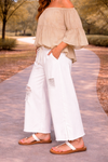side view of woman wearing distressed white wide leg jeans with flowy off the shoulder boho blouse and flat sandals walking outdoors