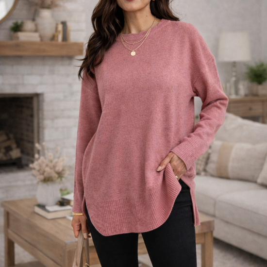 A woman wearing a dusty rose oversized sweater in a cozy living room.