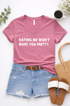 Flat lay of a dusty rose Bella Canvas V-neck graphic tee with “Hating me won’t make you pretty” paired with distressed denim shorts, a brown belt, white slide sandals, and a woven tote